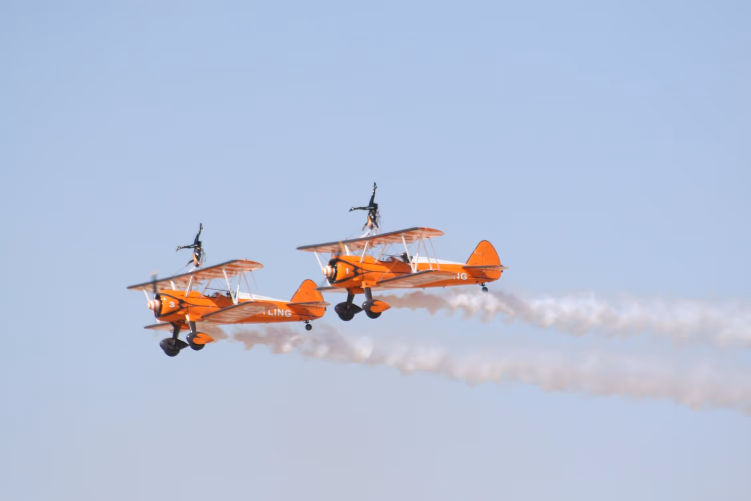 Two biplanes soaring through the air side by side.